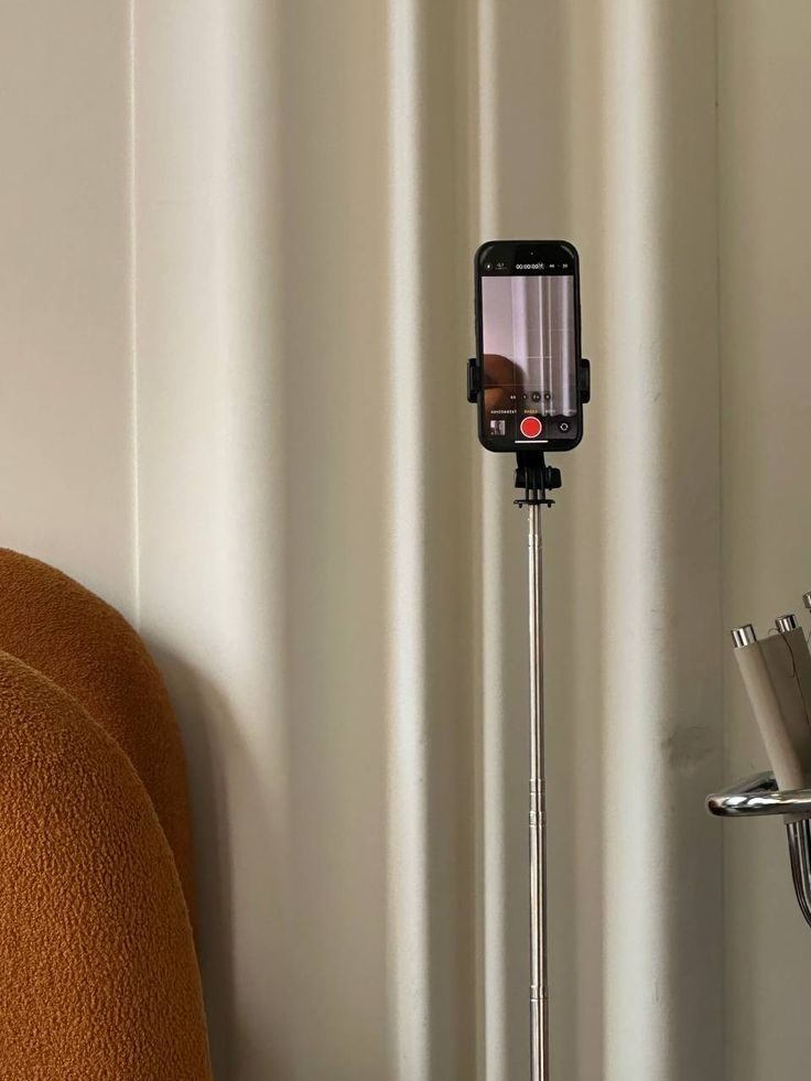 A phone mounted on a tripod recording, against cream curtains